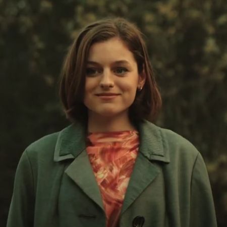 Emma Corrin is smiling looking at something.